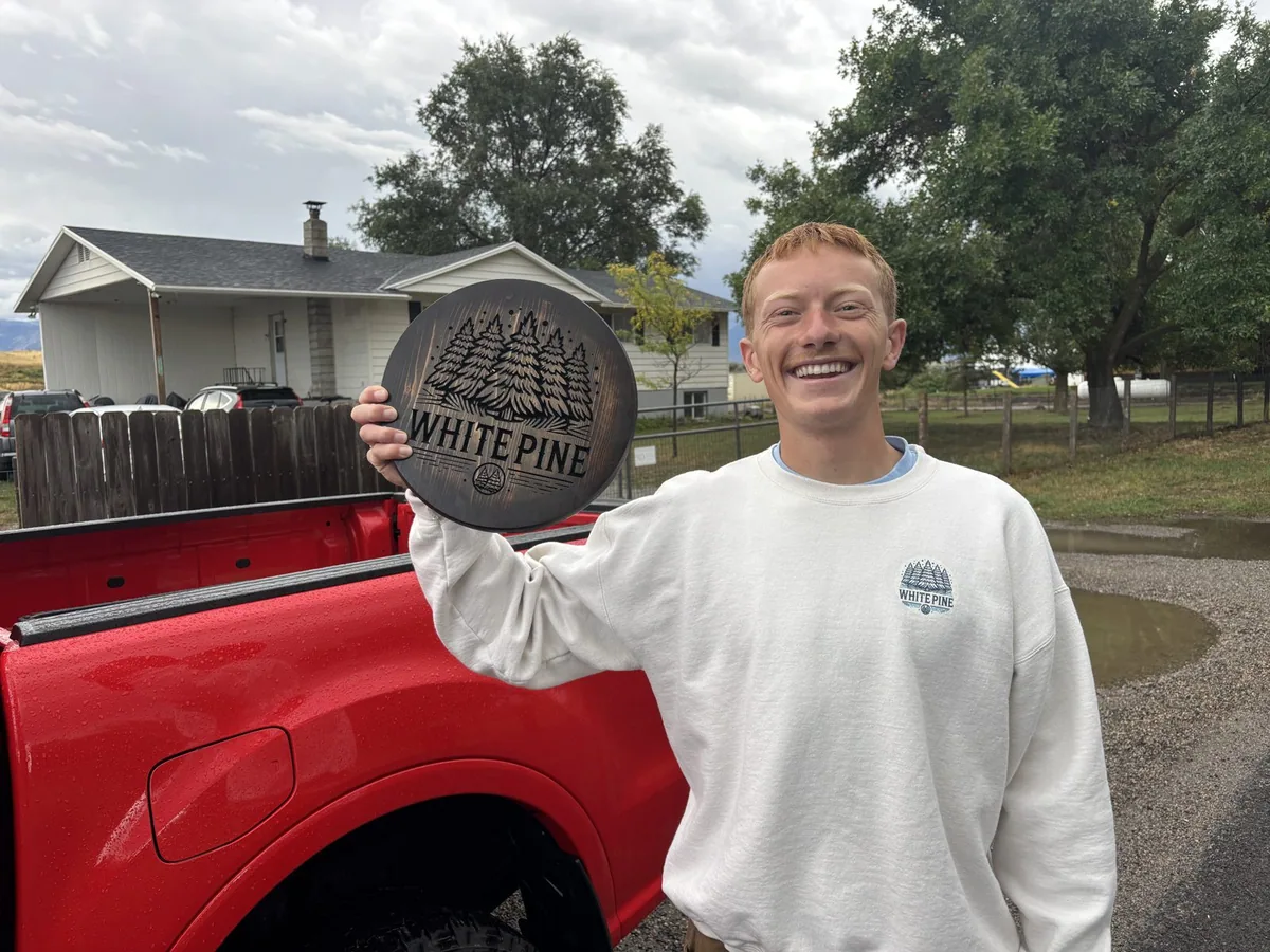 White Pine Roofing team member holding a carved wooden White Pine sign